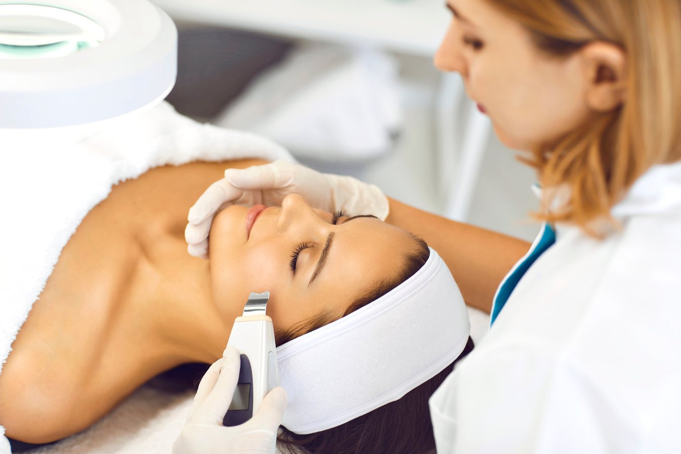 Beautician Makes Facial Cleansing to a Woman in a Beauty Clinic. Ultrasound Procedures for the Treatment of a Woman's Skin